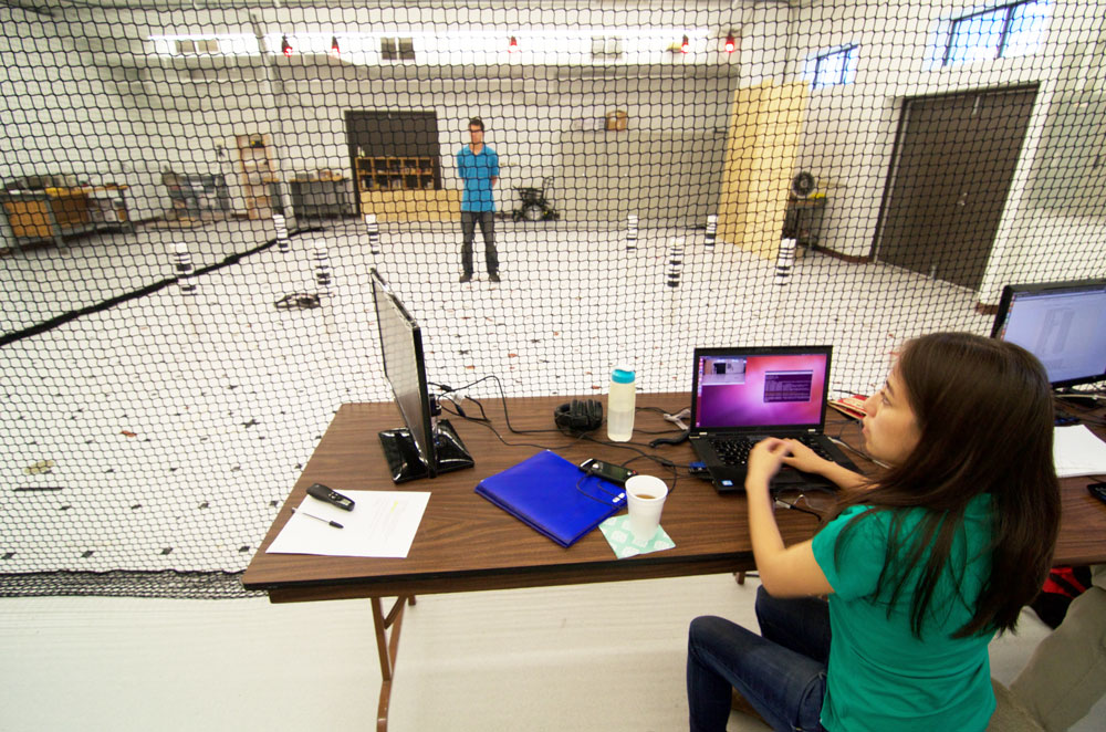 Karime Pereida Pérez launching a flight sequence for an Unmanned Aerial Vehicle (UAV). In the background, Rikky Duivenvoorden awaiting to apply interference forces on the UAV from inside the flying arena. Photo credit: François Pomerleau - University of Toronto.