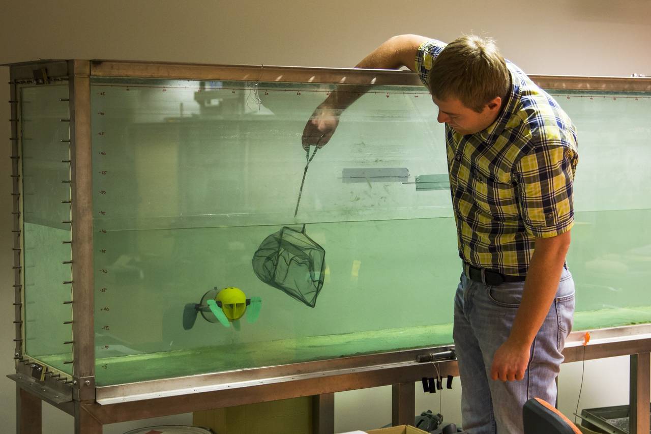 In this photo taken on Wednesday, Nov.  25, 2015, Taavi Salumae, designer of the U-CAT robot and researcher at the Biorobotics Centre at the Tallinn University of Technology, tests the U-CAT robot in an aquarium using a fish net in Tallinn, Estonia. The unique feature of the U-CAT, about the size of a vacuum cleaner, is four silicon flippers inspired by streamlined sea turtles' arms and legs. (AP Photo/Vitnija Saldava)
