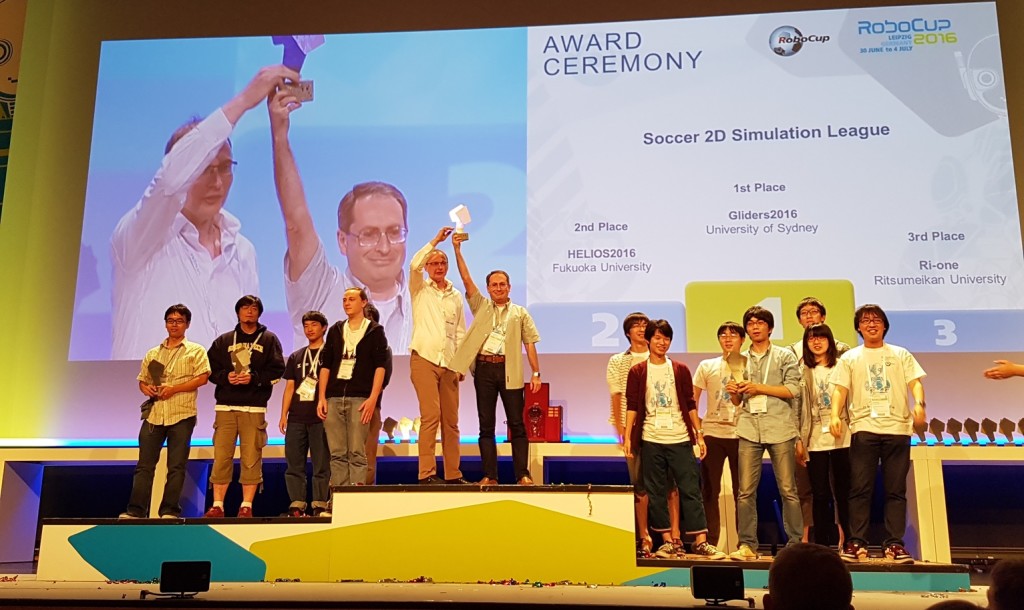 The author (centre podium, right) and Dr Obst (centre podium, left) claim the championship trophy at the 2016 RoboCup award ceremony in Leipzig, Germany. Credit: Natalia Kishigami